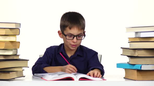 Boy Sits at the Table Leafing Through the Book. White Background