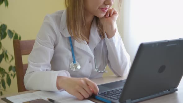 A nurse in a bathrobe and with a stethoscope works at a laptop