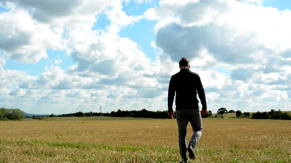 Young Handsome Hipster Man Walks in the Field From Camera To Distance - Cloudy Sky