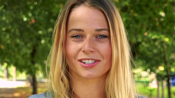 Young Pretty Blond Woman Talks To Camera - Park with Trees in Background - Closeup