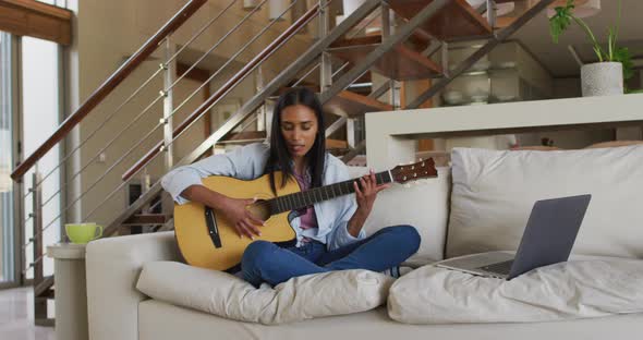 Mixed race woman on couch using laptop playing guitar and singing