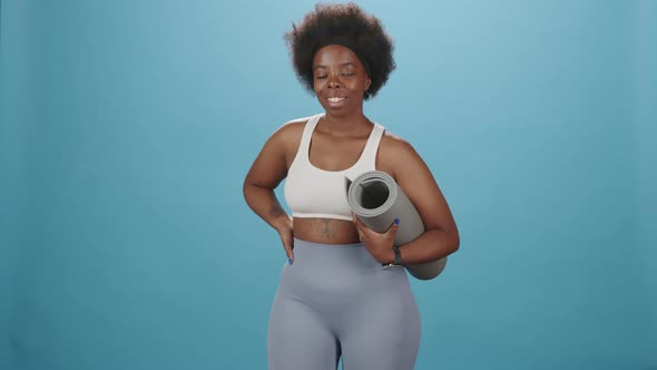 Portrait of Black Plus Size Woman with Yoga Mat on Blue Background