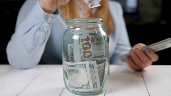 Closeup of Woman Hands Putting Us Dollar Money Into Glass Mason Jar