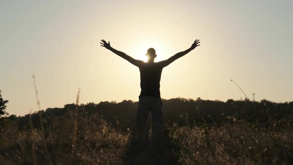 Silhouette of Young Man Against Sunset Raising Hands Sides and Up. Slow Motion