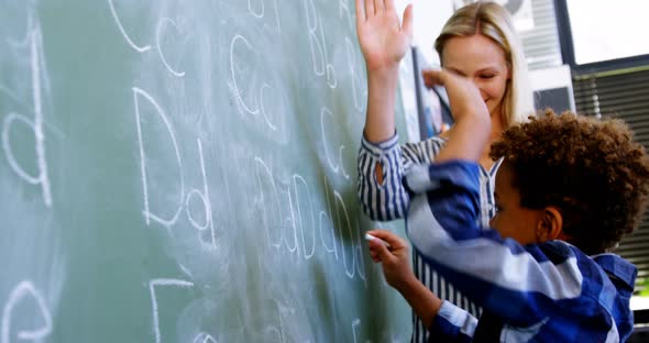 Teacher assisting schoolboy in writing alphabet on chalkboard