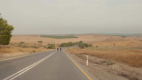 slow motion wide shot of two road cycelist professionals riding in the desert's empty road