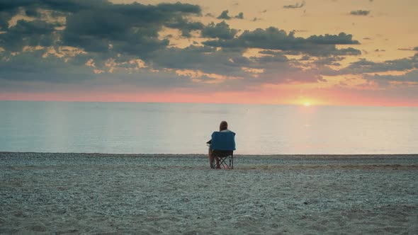 Back View of Woman Admiring Sunset on the Sea Sitting in Folding Tourist Chair