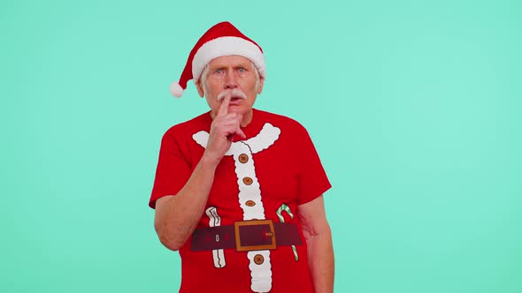 Senior Old Man in Christmas Tshirt Presses Index Finger to Lips Makes Silence Gesture Sign Secret