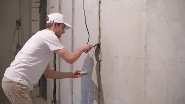 A worker closes a channel with a cement mortar with a cable in the wall