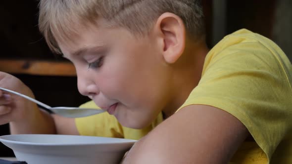 Closeup of a Teenage Boy in a Yellow Tshirt Eats Soup with a Spoon From a Bowl