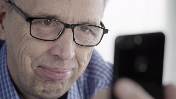 Man With Glasses Looks at the Smartphone Screen and Smiles