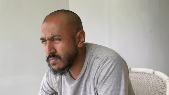 View Of Asian Bangladeshi Male Sat Down Looking Outward Thinking With White Wall Background. Dolly S