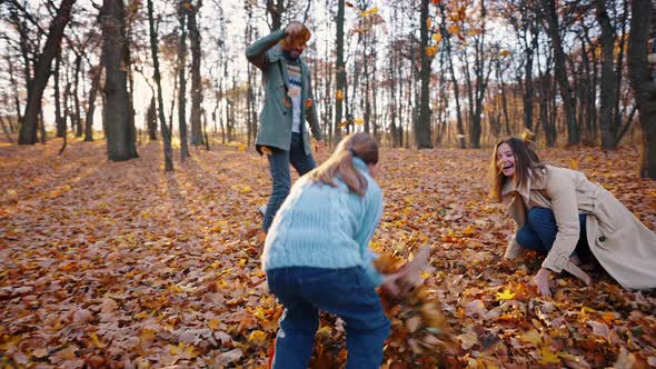 Young Mom Dad and Little Daughter Laughing and Throwing Yellow Leaves at Each Other Playing in