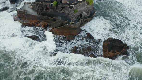 Aerial View of Dangerous Rocks and Strong Waves Crashing Into Off Shore Cliff with Tanah Lot Temple