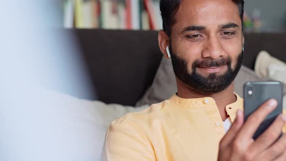Indian Man Sitting at Home on Sofa Using Mobile Phone Watching Videos