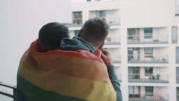 Young Homosexual Couple Enjoying the View From the Balcony Covered with Pride Rainbow Flag