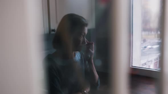 Lonely Elderly Woman Wiping Her Tears While Looking Through the Window in the Kitchen