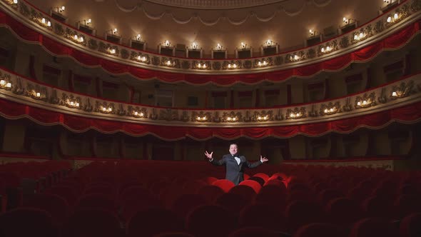 Actor among red seats in empty concert hall.