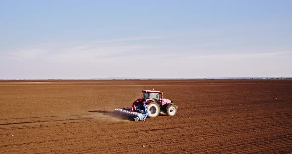 Farmer seeding soybeans with tractor on plowed field