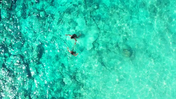 A pair of young female friends on vacation enjoying a relaxing swim in the crystal clear waters in F