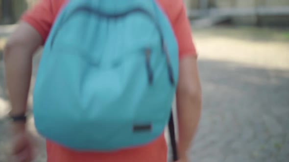 Back View of Schoolboy with Backpack Running Along Sunny Schoolyard Outdoors. Blond Positive