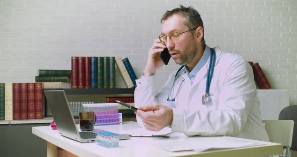 Dolyy Shot of a Middleaged Doctor is Talking to a Patient on the Phone