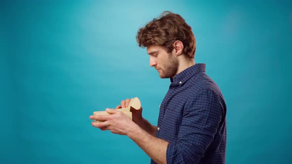 Young Casual Bearded Man Opening Cardboard Box Against Blue Background