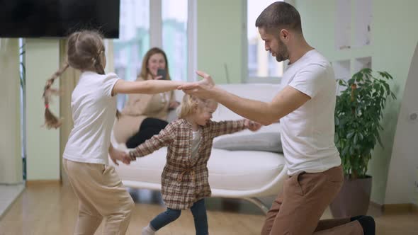 Happy Father Having Fun with Daughters Dancing in Slow Motion As Cheerful Mother Taking Video on