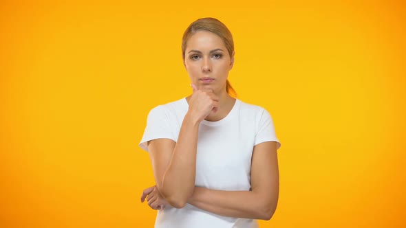 Thoughtful Female With Hand on Chin Standing on Orange Background, Hesitation