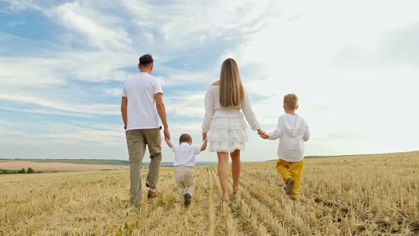 Family with Children Walks Joining Hands on Mown Wheat Field