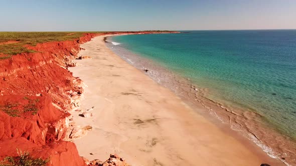 Aerial footage of male and female couple sitting atop red cliff overlooking beach and blue ocean
