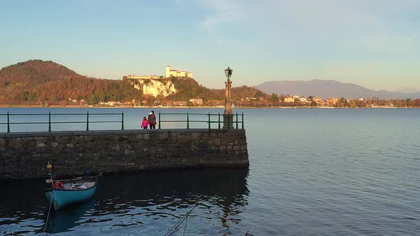 Mother and daughter walk on waterfront pier on  Lake Maggiore with Angera fortress in background