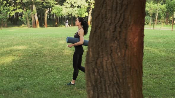 Young Pretty Woman Rolling Blue Yoga Mat or Fitness Mat Prepare to Exercise in Park