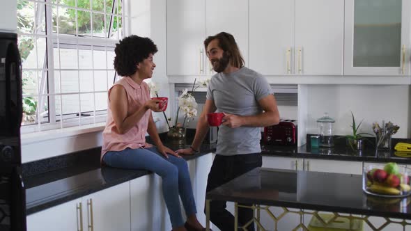 Mixed race couple holding coffee cup talking to each other in the kitchen at home