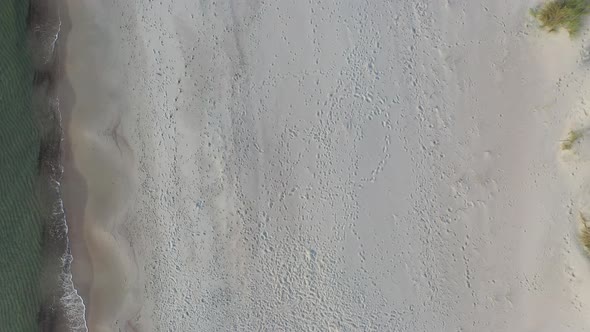 AERIAL: Top View Pan Shot of Sandy Beach with Foot Prints and Waves Crashing on a Shore