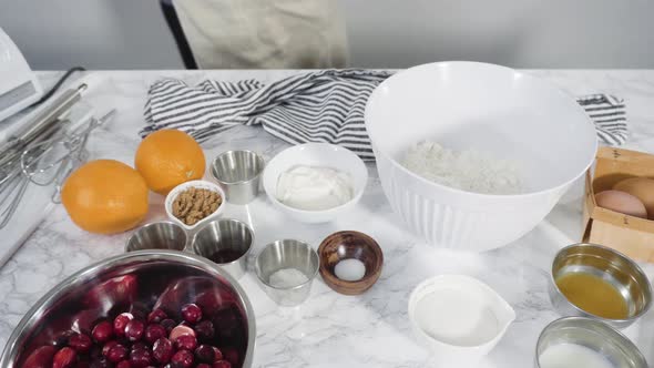 Step by step. Ingredients to bake cranberry muffins on a marble kitchen surface.