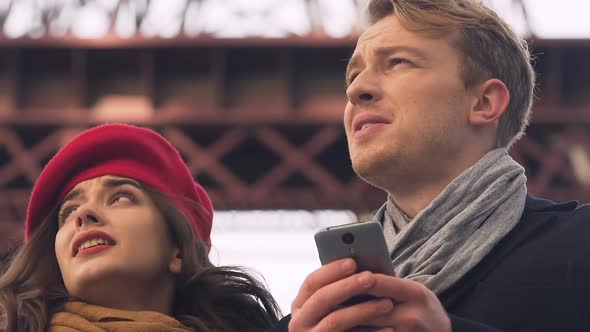 Young tourist couple looking map in cell phone app, get lost in unknown city