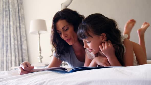 Mother and daughter reading a book while lying on bed in bedroom