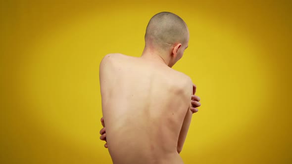 Back View of Young Man Hugging Himself Standing at Yellow Background