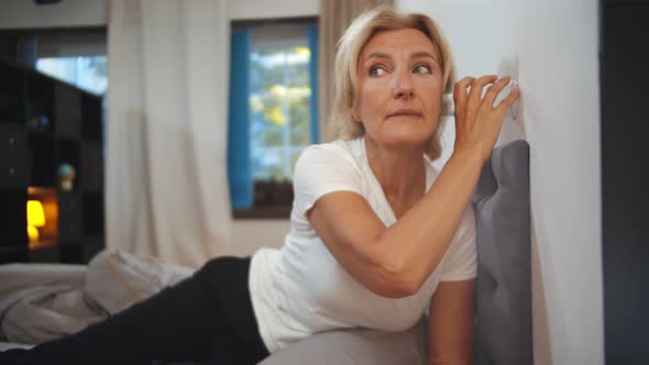 Senior Woman Eavesdropping Through Wall of Room Through Glass Cup