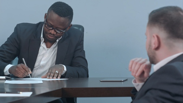 Black businessman signs a contract and gives papers to a partner