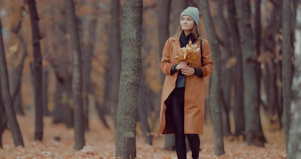 Girl in the Autumn Forest with a Bouquet of Orange Leaves