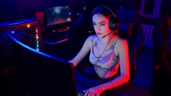 Gaming Concept - Young Attractive Woman Sits in the Chair in Neon Gaming Club and Playing Games