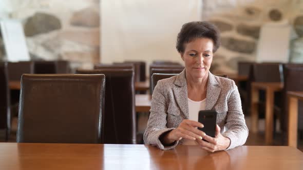 Happy Mature Businesswoman Thinking While Using Phone At The Coffee Shop