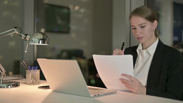 Gorgeous Businesswoman Reading Document on Office Desk at Night