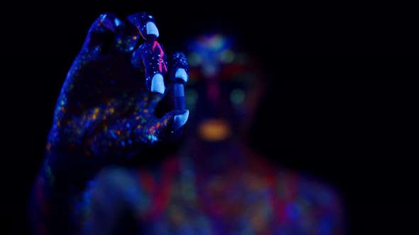 Woman Painted in Different Luminous Fluorescent Paints Holds Pill and Eats It Dark Background Front