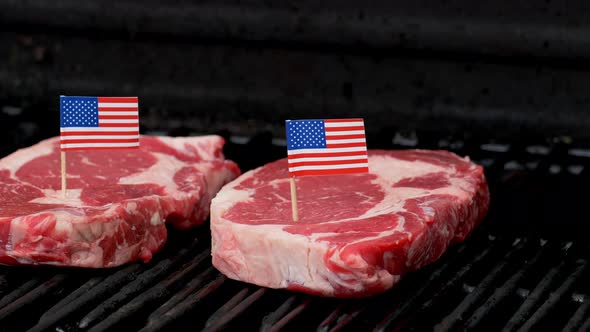 Two juicy rib-eye steaks sitting on the grill and cooking with two tiny American flags tooth picked