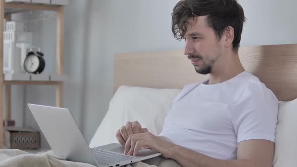 Online Video Chat By Excited Man Lying on Stomach in Bed