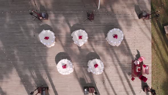 Aerial View of Round White Tables with Red Flowers on Wooden Platform in Forest