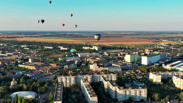 Multicolored balloons fly over fields, houses, trees. Blue sky.